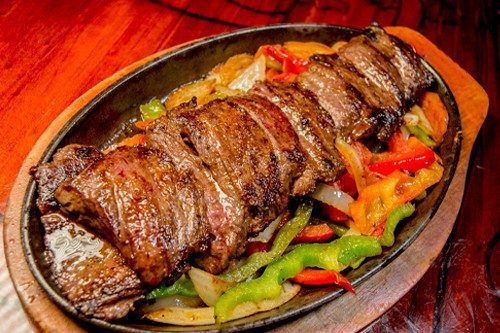 Corte a la parrilla con papas y verduras asadas, servido sobre piedra volcánica